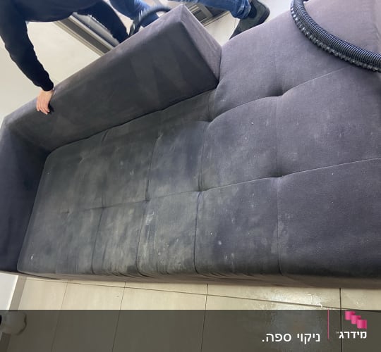 אדם מנקה ספה כהה עם שואב אבק
